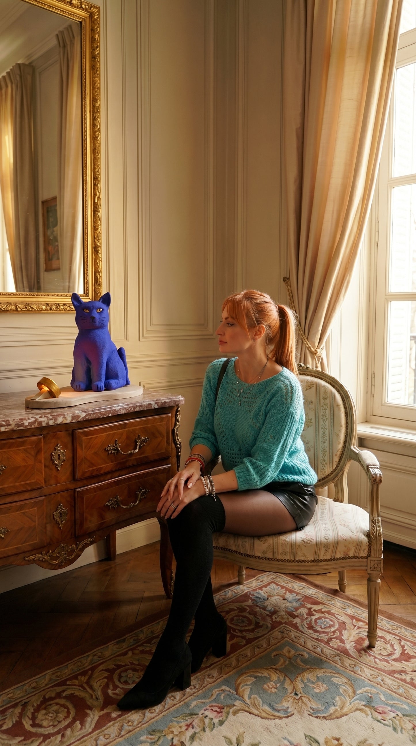 Woman sitting on a chair in an elegant room with a blue sculpture on a table.