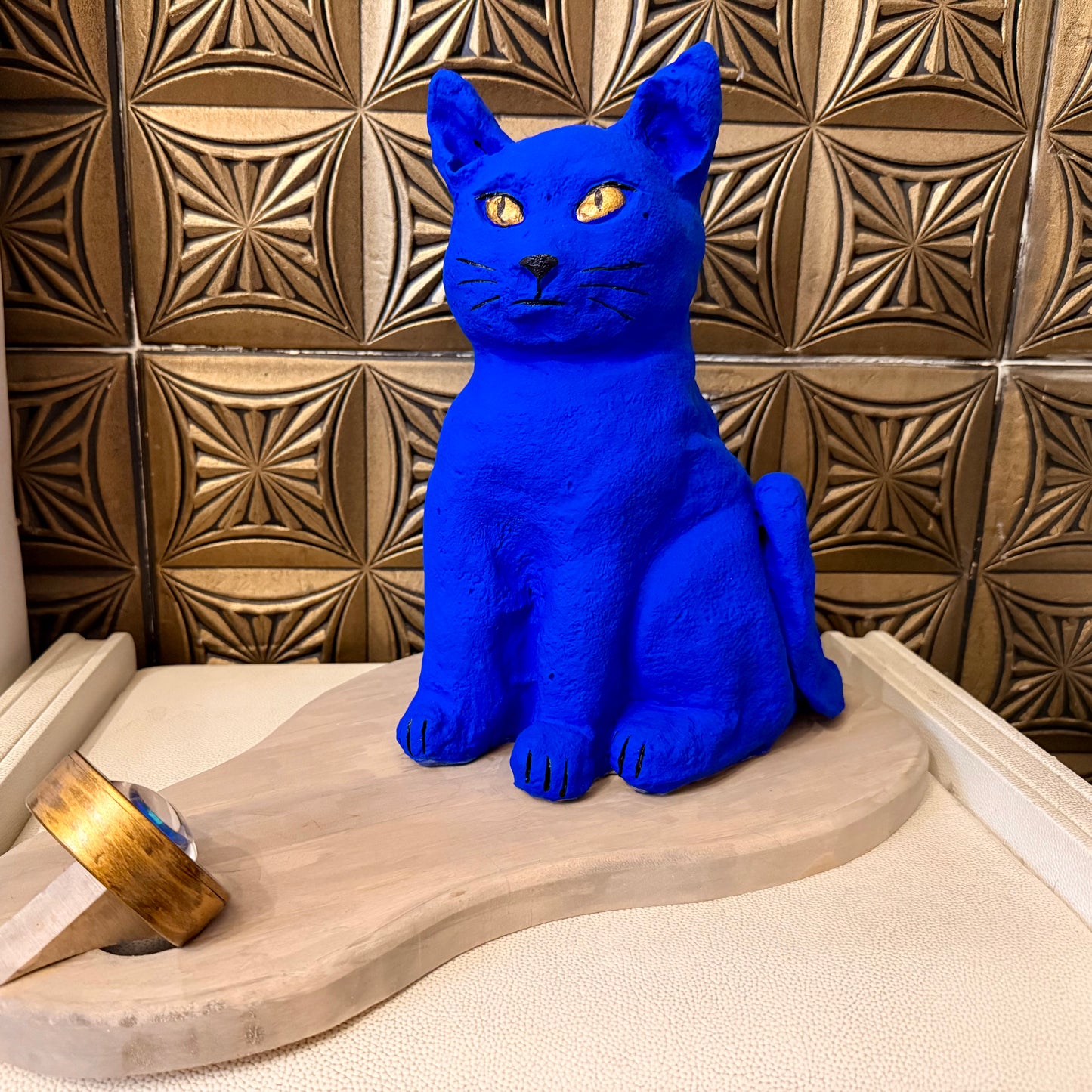 Blue cat statue on a wooden platform with a patterned wall in the background