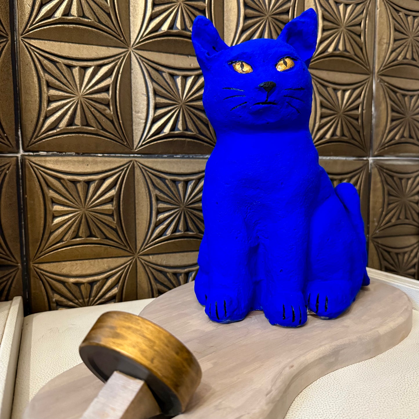 Blue cat figurine on a wooden stand against a decorative tiled wall.