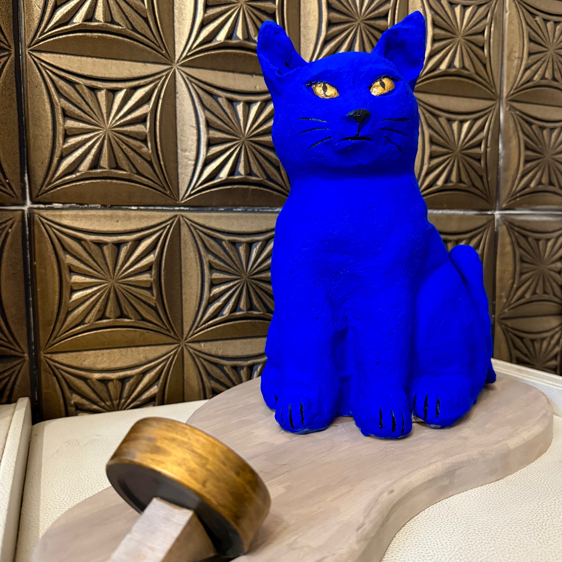 Blue cat figurine on a wooden stand against a decorative tiled wall.