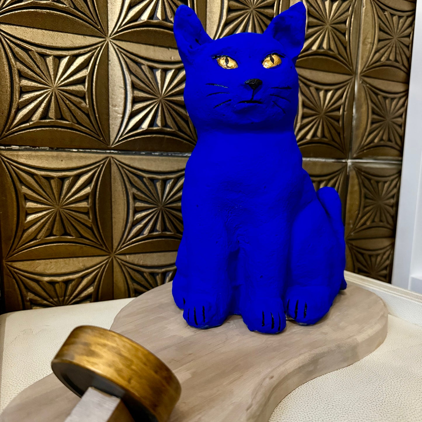 Blue cat figurine on a wooden surface with a decorative tiled wall in the background