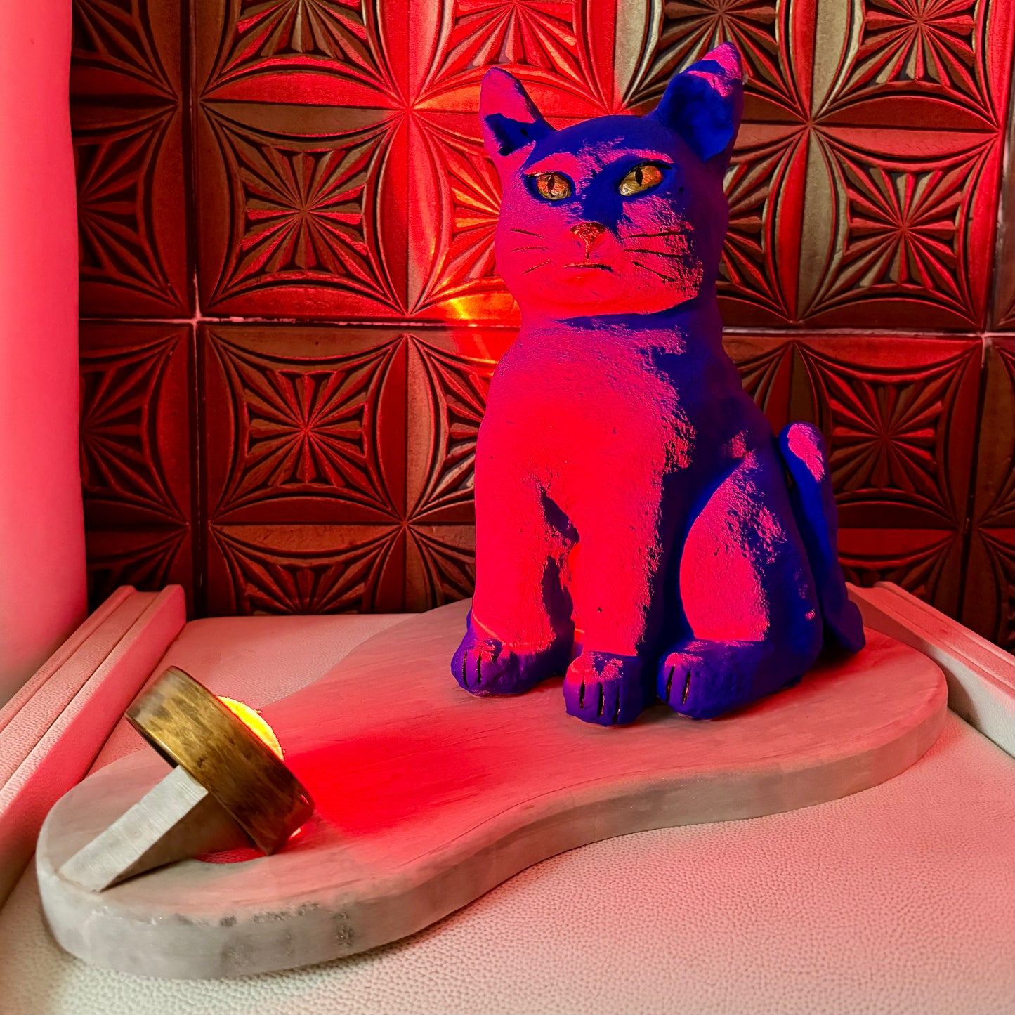 Colorful cat-shaped lamp on a wooden base with a red-tinted wall in the background