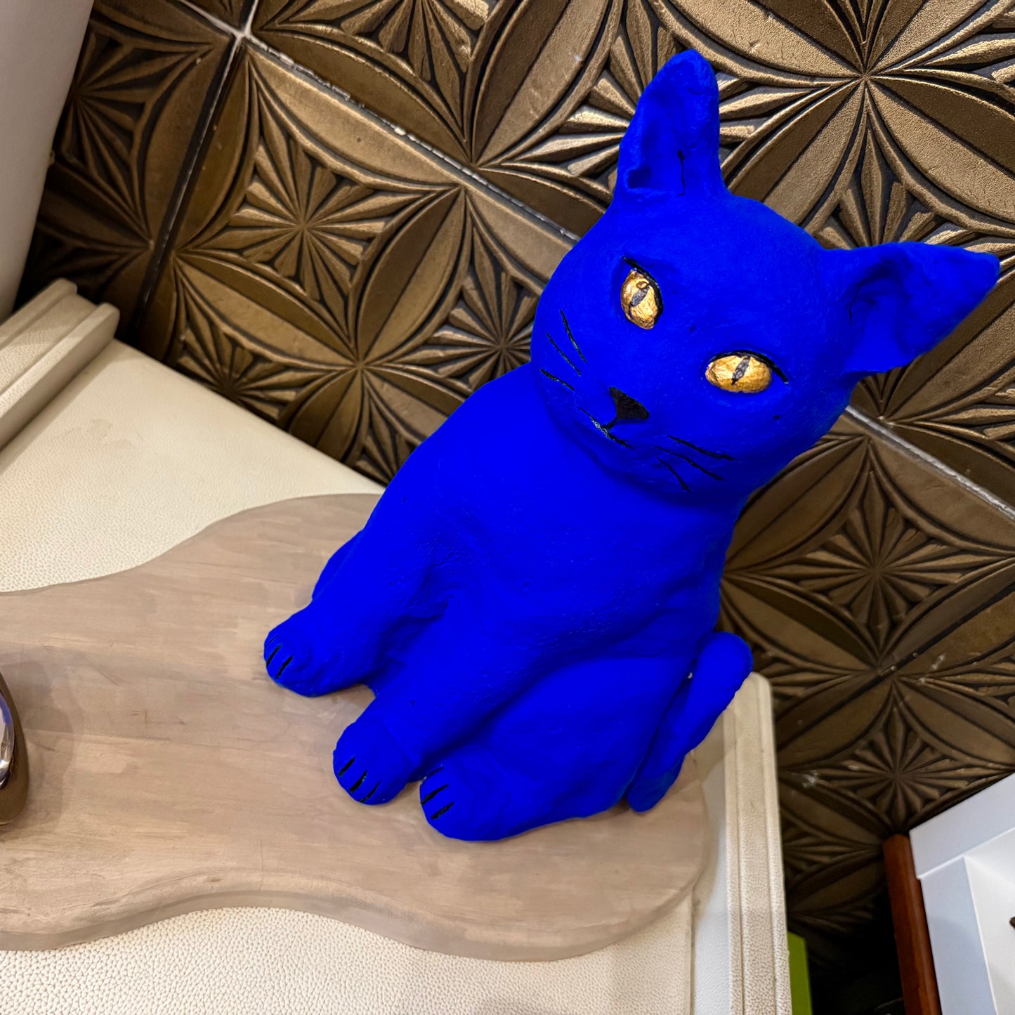 Blue cat-shaped object on a wooden surface with a decorative wall in the background
