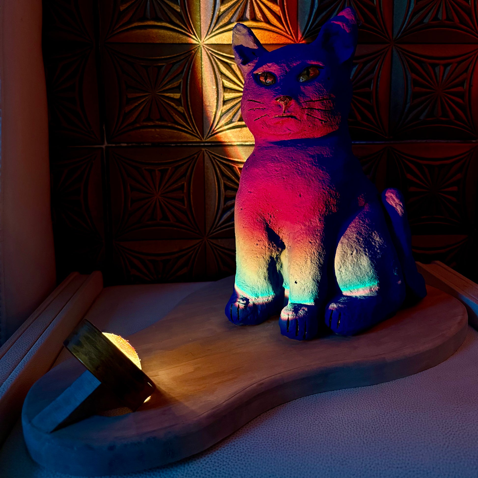 Colorful cat-shaped lamp on a wooden surface with a patterned wall in the background