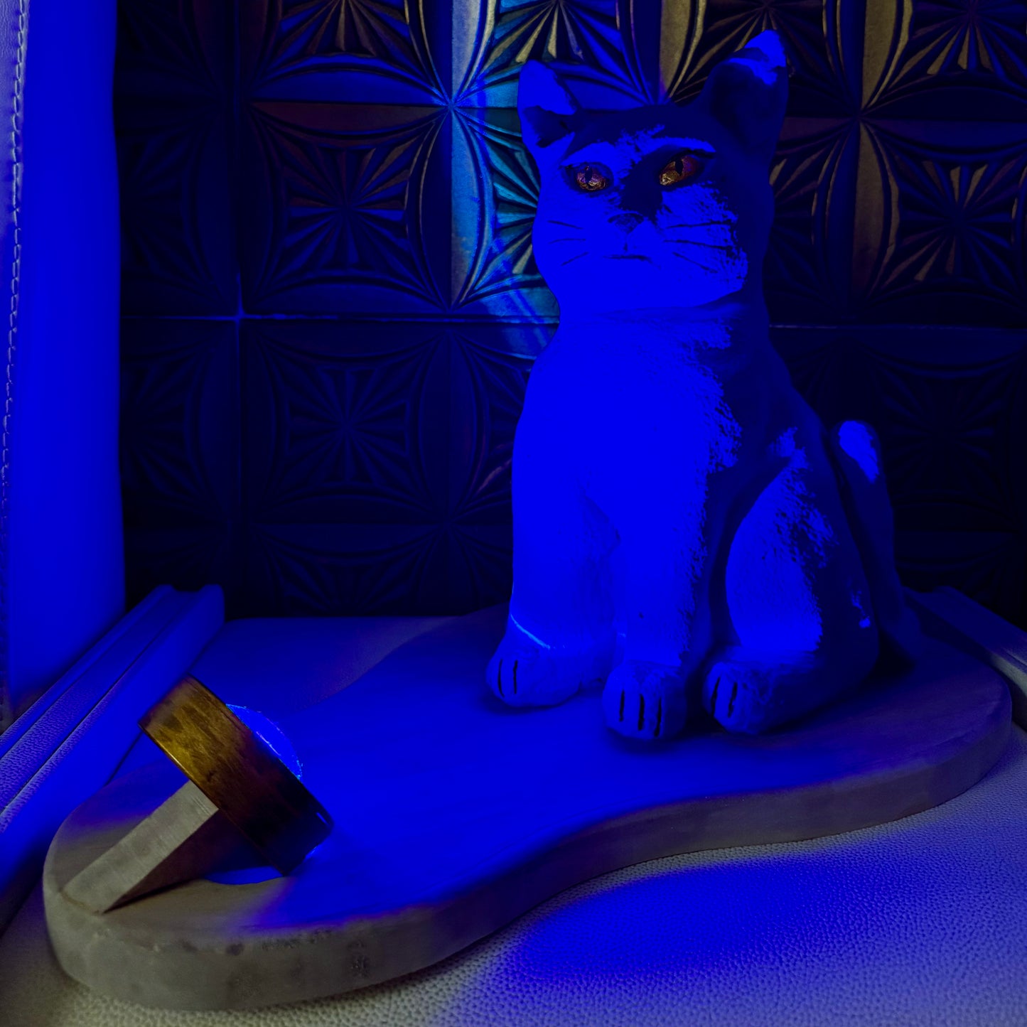 Blue cat-shaped lamp on a wooden base with a dark patterned wall in the background