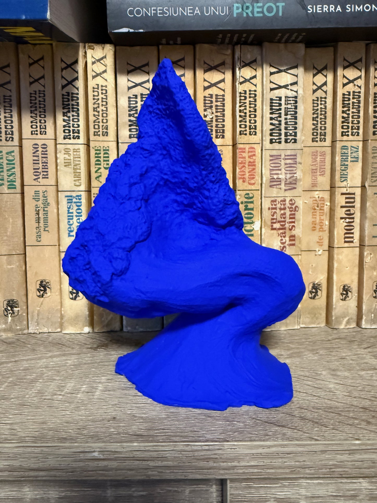 Blue 3D-printed figure on a wooden surface with stacked books in the background