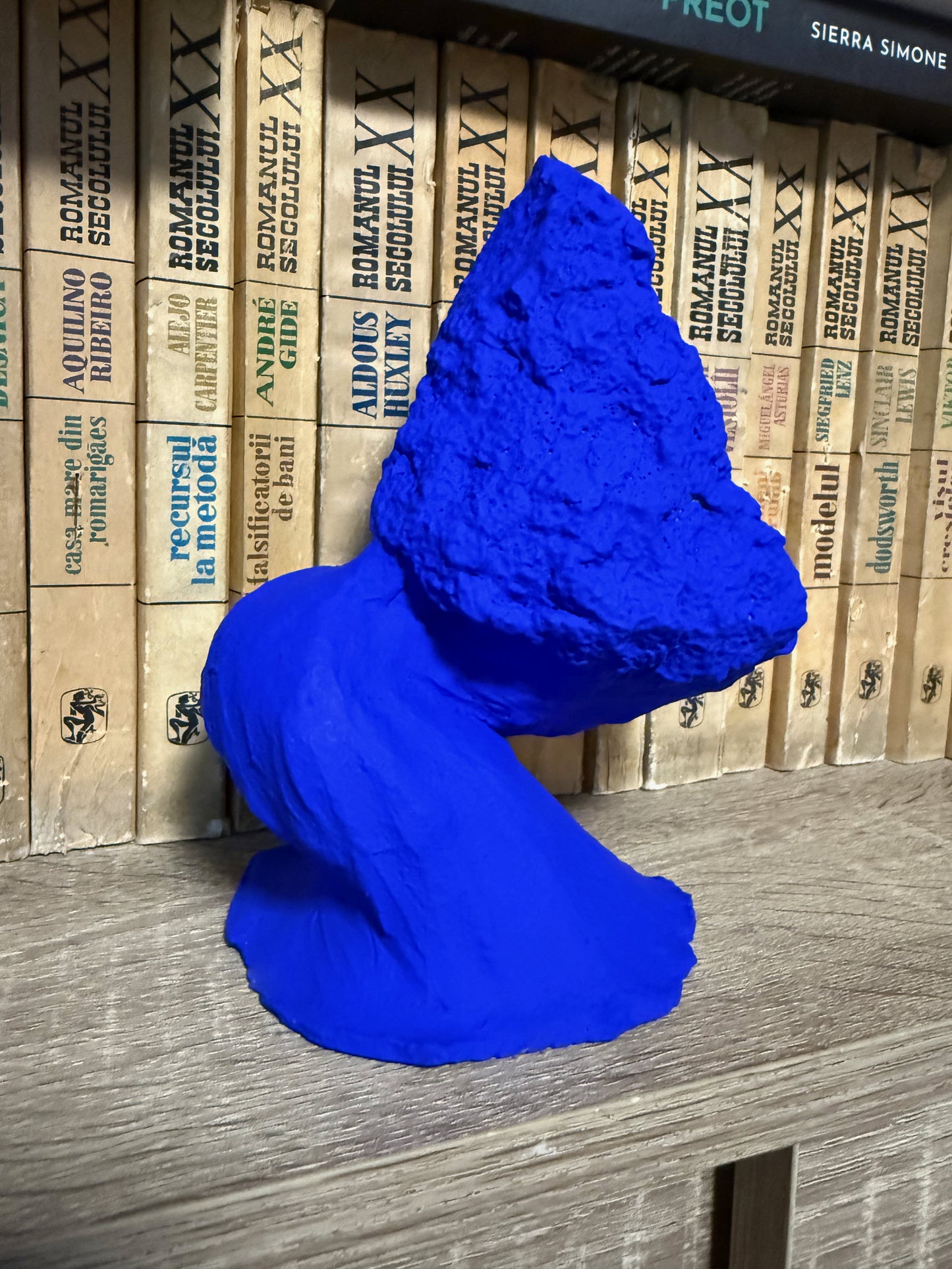 Blue sculpture on a wooden surface with stacked books in the background