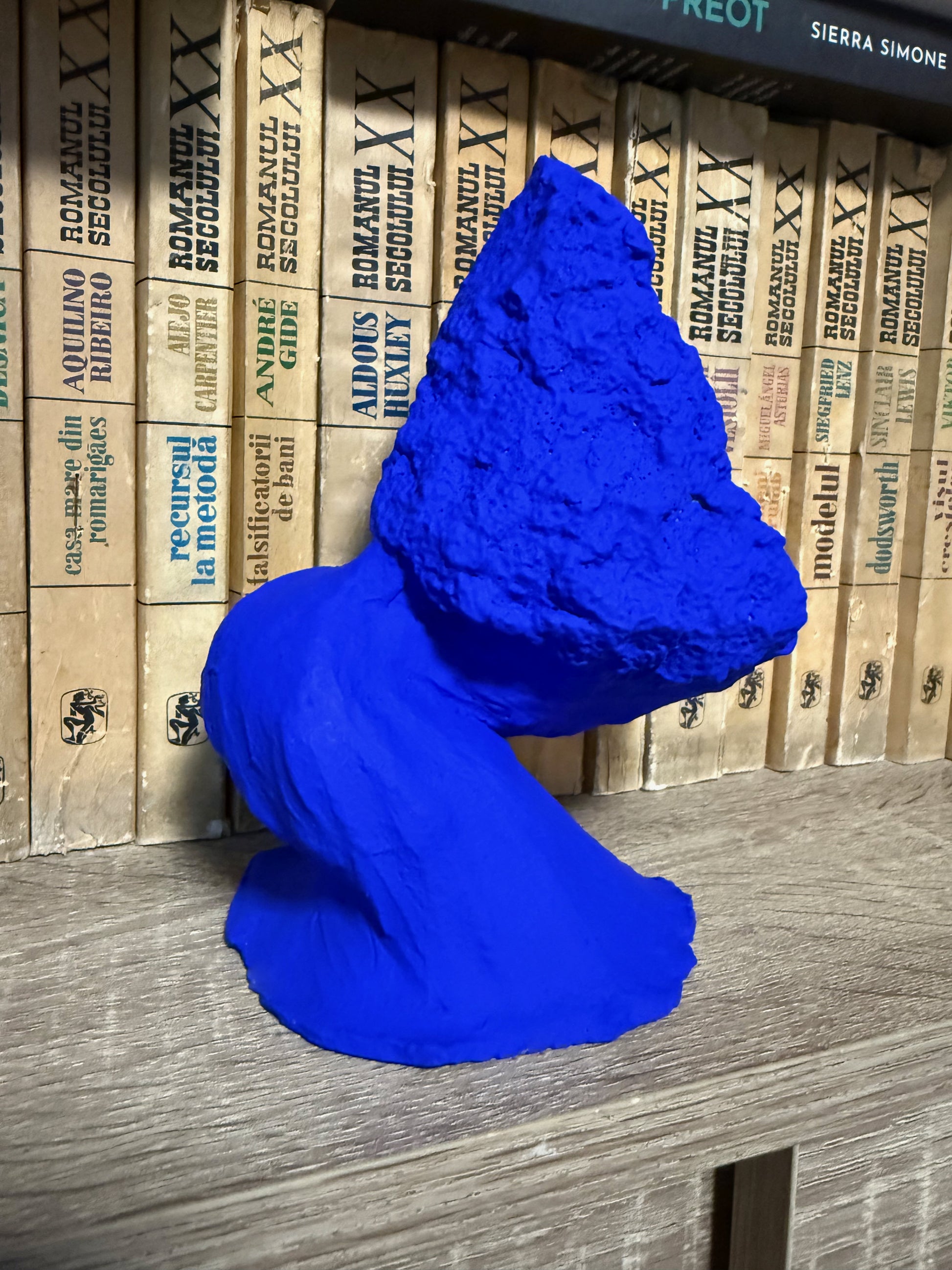 Blue sculpture on a wooden surface with stacked books in the background