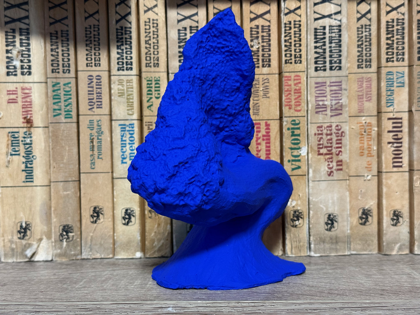 Blue sculpture in front of stacked books with visible text