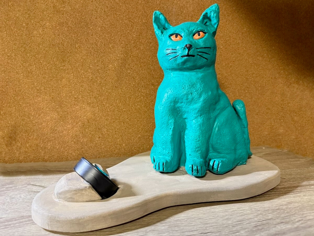 Turquoise cat figurine on a wooden stand with a brown background