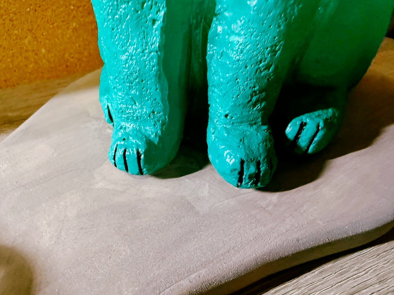Teal ceramic bear figurine on a stone surface with a wooden background