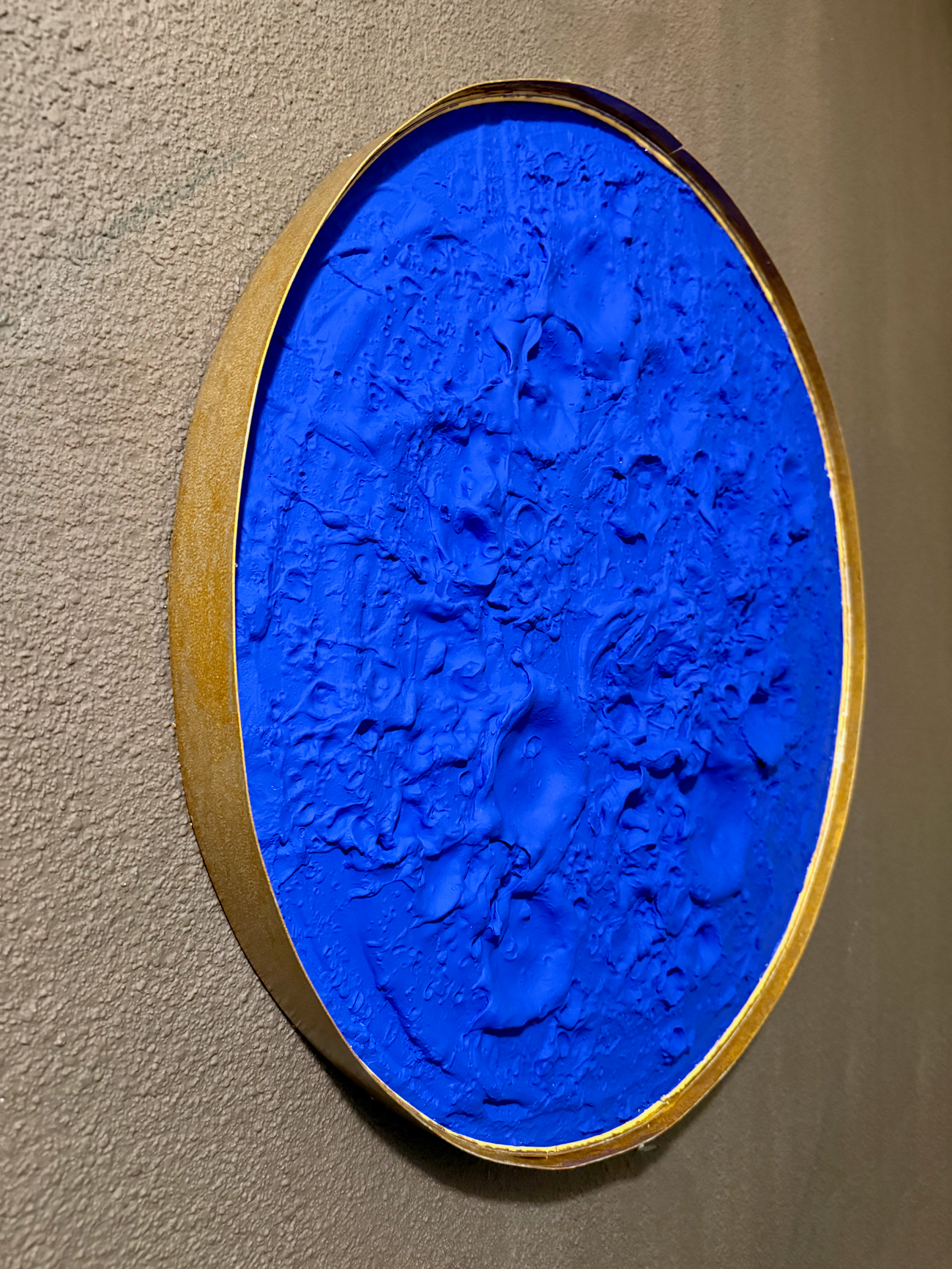 Blue textured artwork in a gold frame on a beige wall