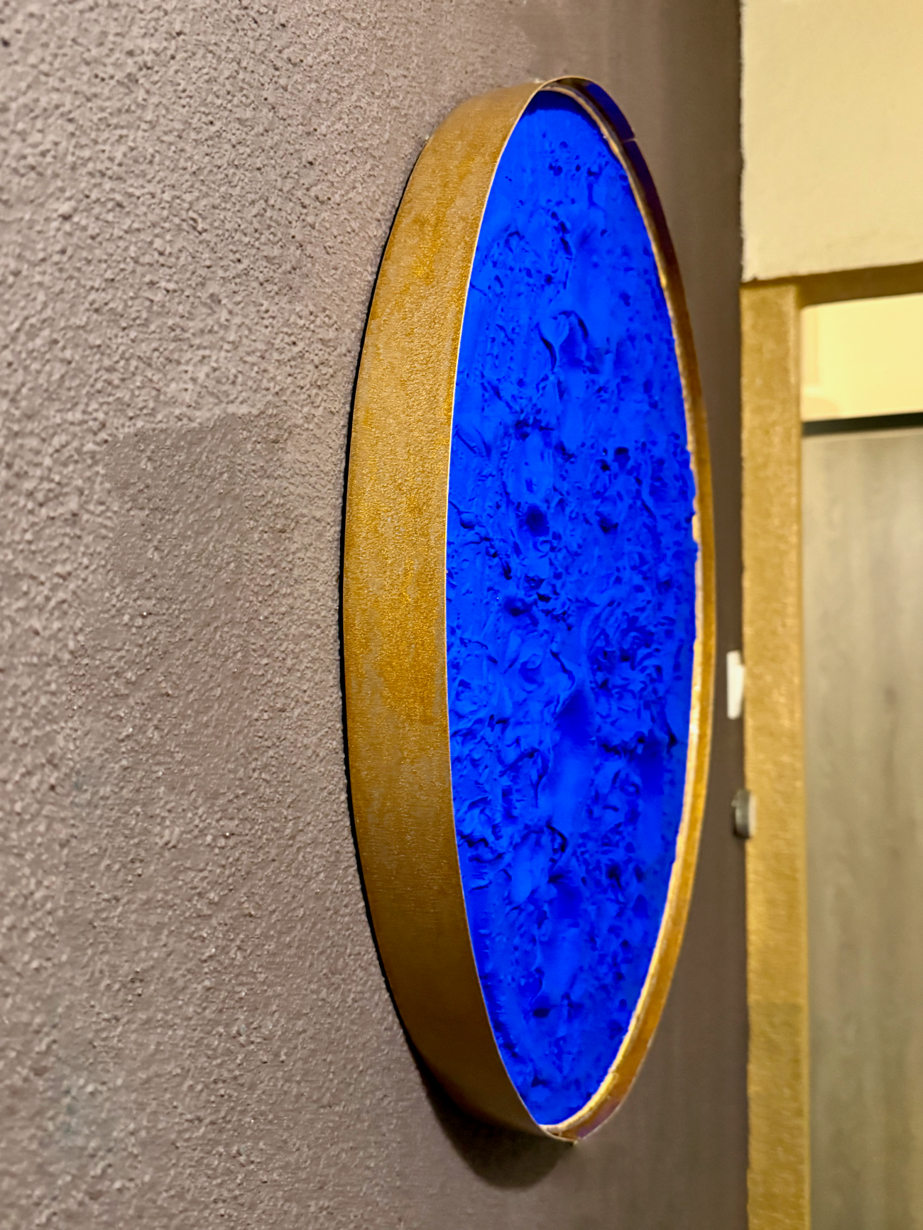 Round blue light fixture with wooden frame on a gray wall