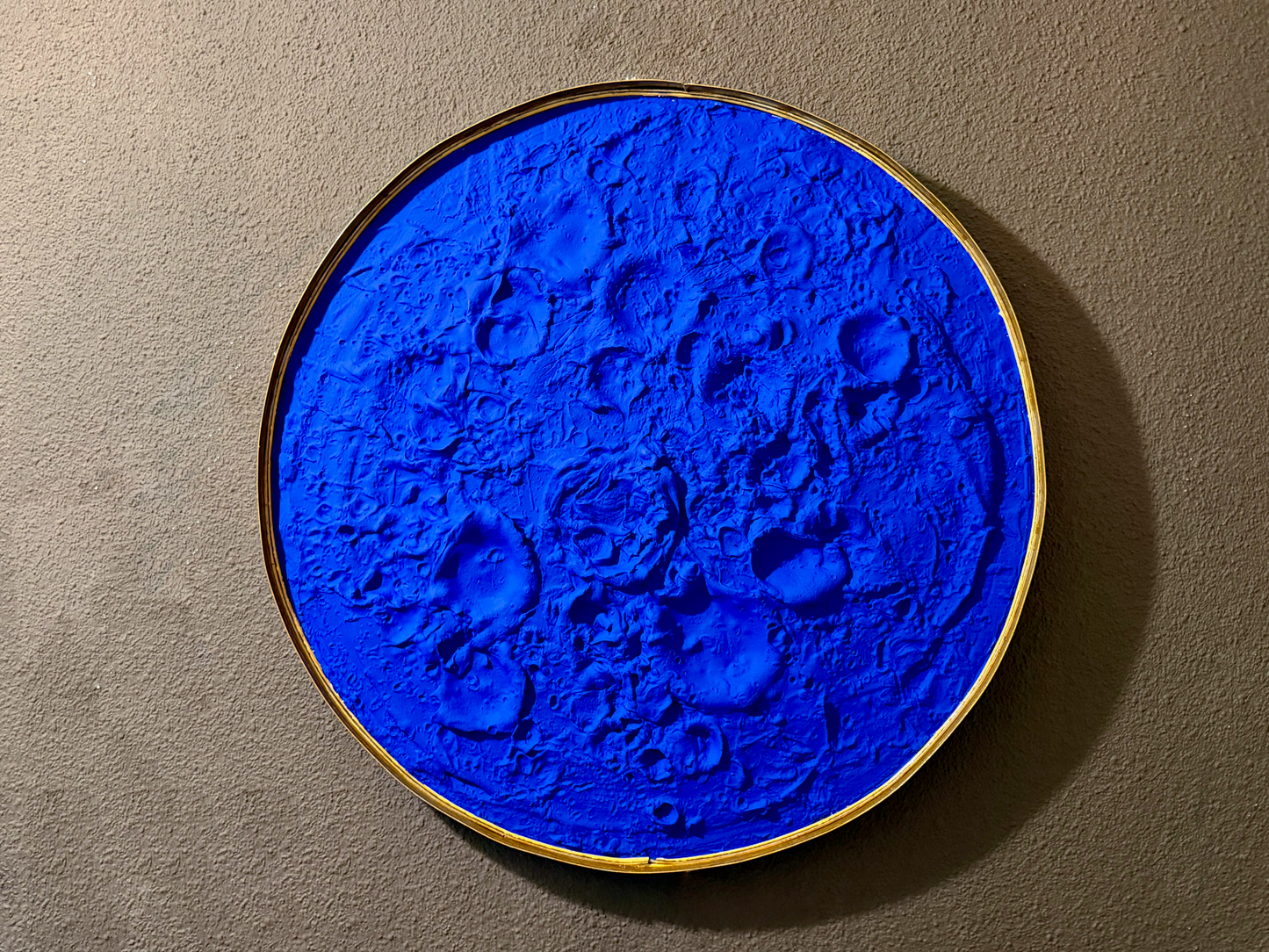 Blue textured circular artwork on a beige wall